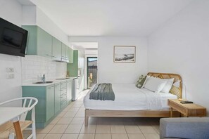 A compact room with a bed, a small table, a chair, a kitchenette, and a television. - Murrays Beach Studio (Sawtell)