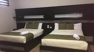 Dos camas individuales con ropa de cama verde, un cabecero oscuro y una ventana con persianas.