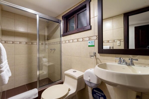 Un baño con cabina de ducha de vidrio, inodoro, lavamanos con espejo y un cartel que indica zona de depósito.