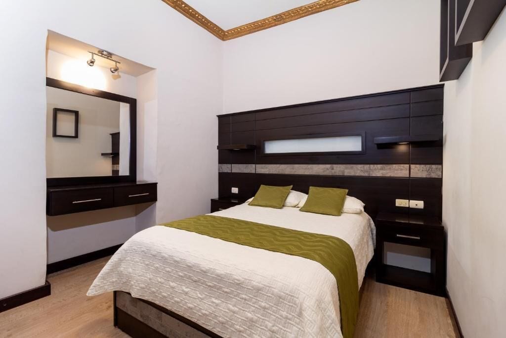 Un dormitorio con cama, mesitas de noche, cómoda, espejo y estante en la pared.