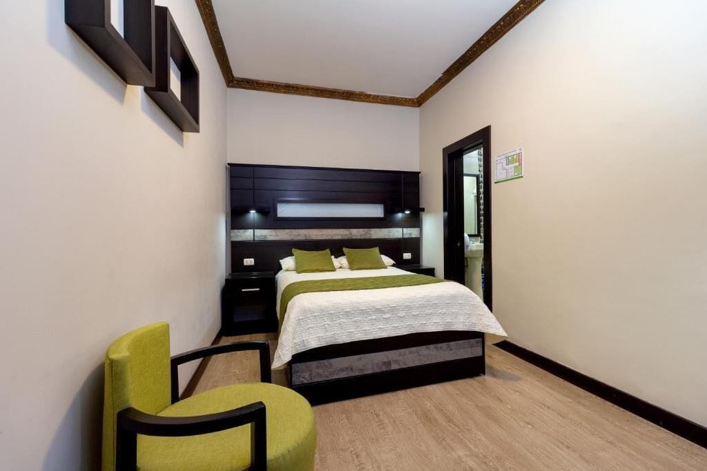 A bedroom with a bed, bedside tables, a chair, and a wall-mounted shelf.
