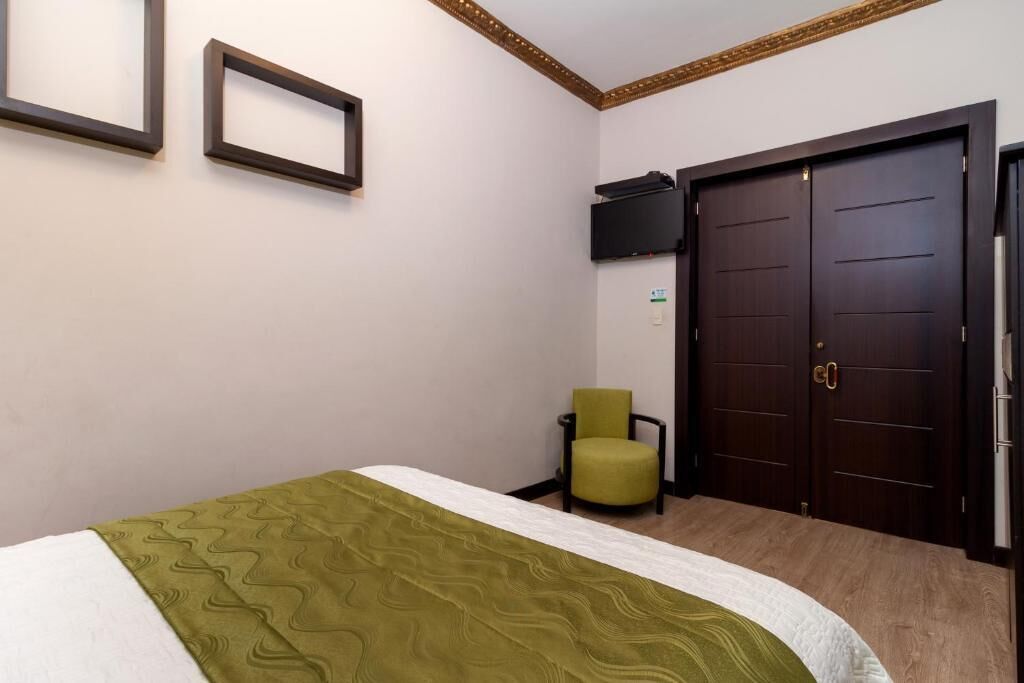 Een hotelkamer met een bed, een groene stoel, een televisie en een dubbele deur.