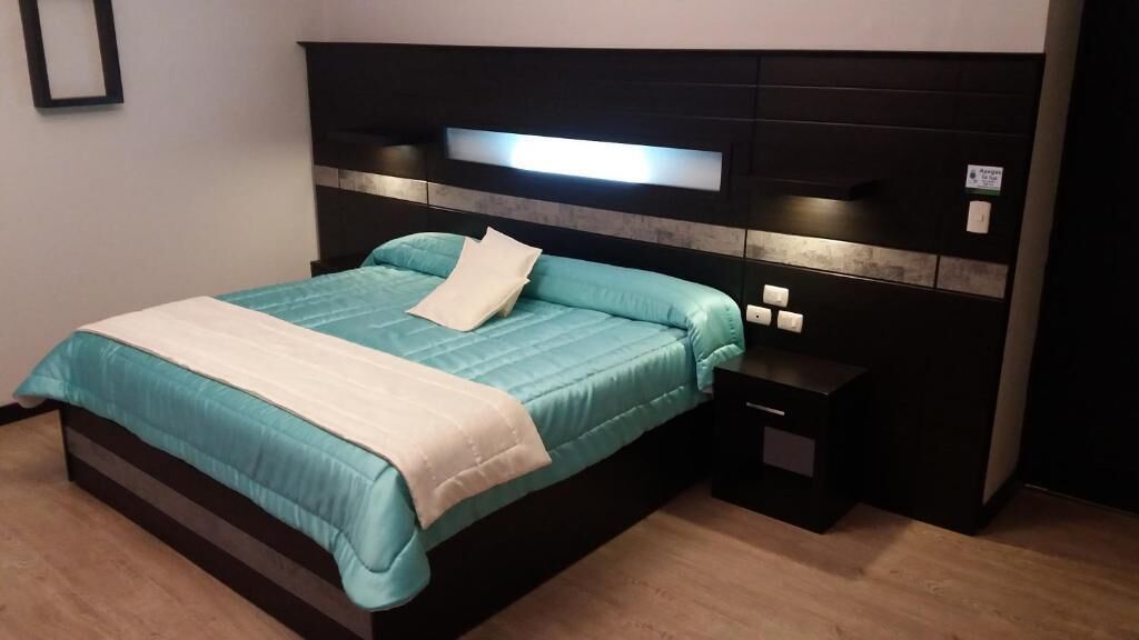A modern hotel room with a large bed, a bedside table, and a headboard with built-in lighting.