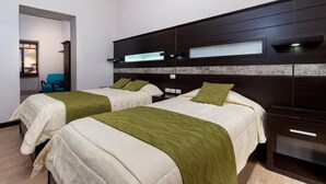Habitación de hotel con dos camas, cabecera oscura y una pequeña zona de estar con una silla.