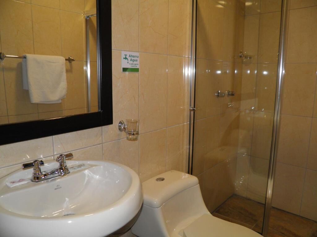 Un baño con lavamanos blanco, espejo y ducha con mampara de vidrio.