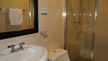 Un baño con lavamanos blanco, espejo y ducha con mampara de vidrio.