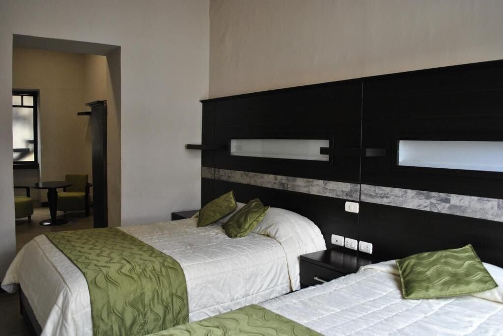 Une chambre d’hôtel avec deux lits, une tête de lit noire et une petite table avec des chaises.