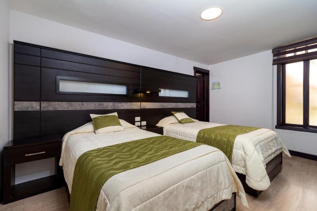 Habitación de hotel con dos camas, cabecera oscura y ventana con persianas.