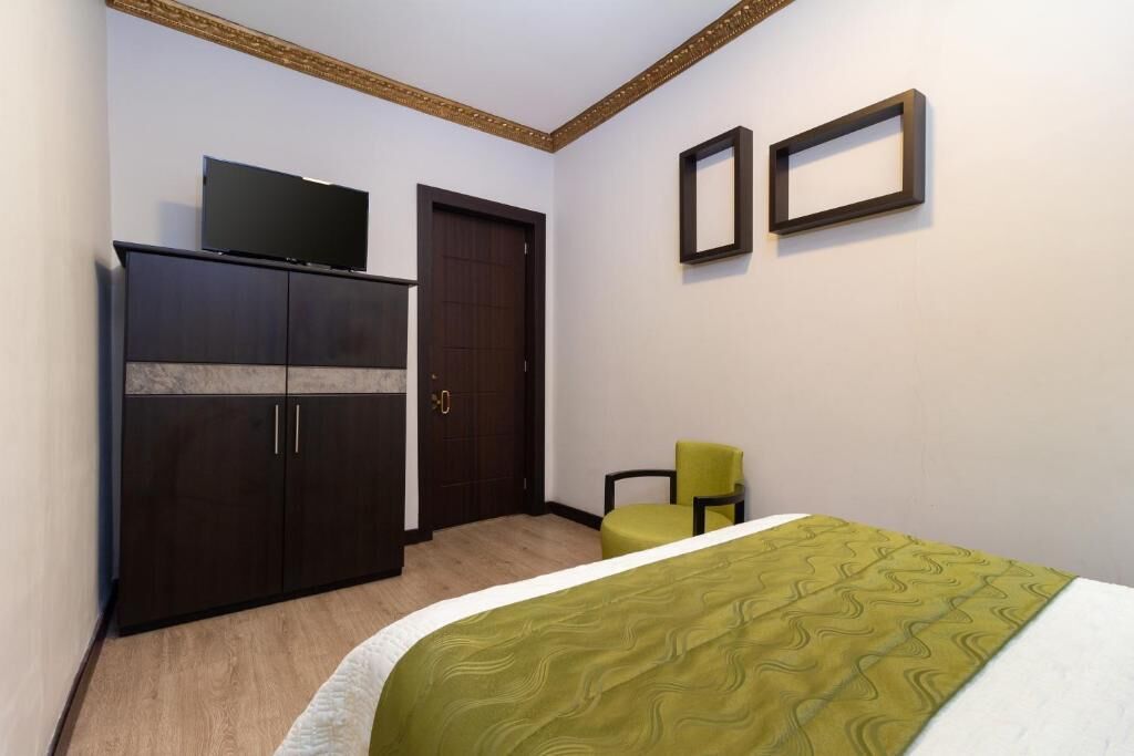 Ein Schlafzimmer mit einem Bett, einem Kleiderschrank, einem Fernseher darauf, zwei gerahmten Bildern an der Wand und einem Sessel.