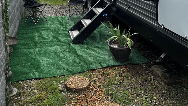 Een caravan met een patio van kunstgras, een geel surfboard en een plant in pot.