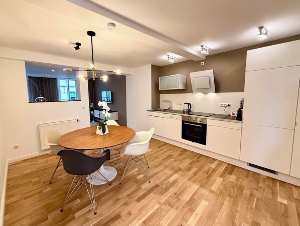 A modern kitchen with white cabinets, a built-in oven, and a dining area with a round wooden table and two chairs. - High-End Designer Living on Dalberg with a Patio (Aschaffenburg)