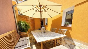 Une terrasse avec une table et des chaises en bois, un grand parasol et des plantes en pot.