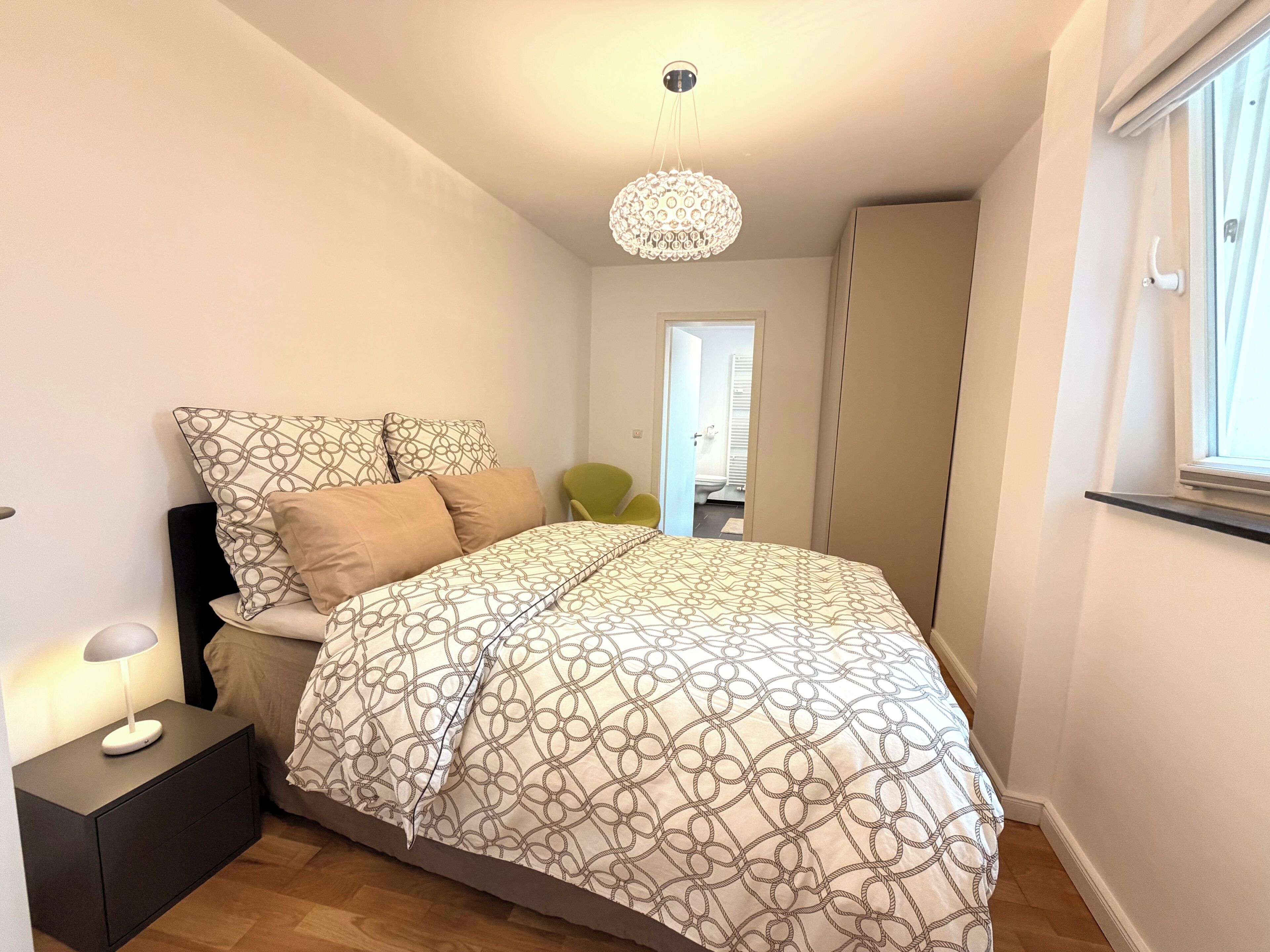 Ein Schlafzimmer mit Bett, Nachttisch, Lampe und einer Pendelleuchte.