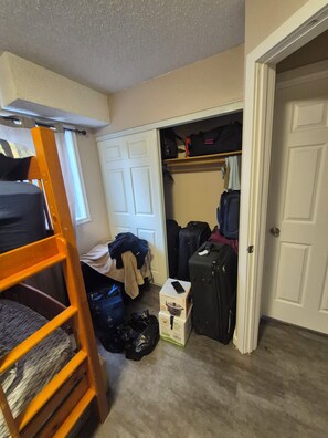 Ein Zimmer mit einem Etagenbett, einem Kleiderschrank mit Kleidung und einem Koffer auf dem Boden.