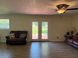A living room with a brown leather sofa, a ceiling fan, and a view through a glass door to a green outdoor area. - Tremendous 5-bedroom house in Groves perfect for group stays (Groves)
