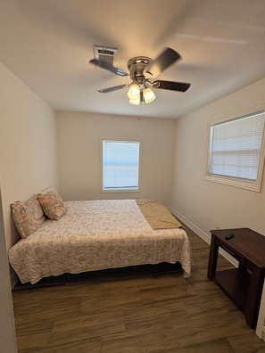 A bedroom with a bed, a ceiling fan, two windows with blinds, and a small table. - Tremendous 5-bedroom house in Groves perfect for group stays (Groves)