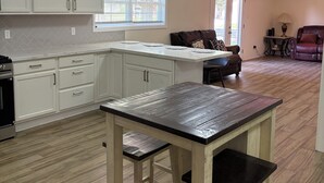 Una cocina con armarios blancos, una mesa de madera y una zona de comedor con un sofá y una lámpara.
