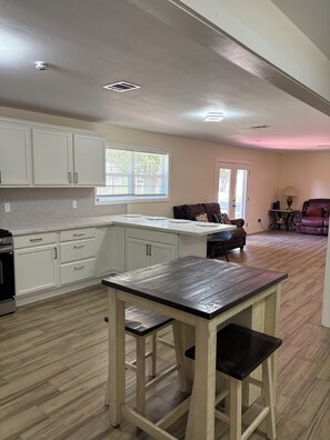 A kitchen with white cabinets, a wooden table, and a dining area with a couch and a lamp. - Tremendous 5-bedroom house in Groves perfect for group stays (Groves)