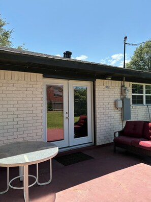 A patio area with a table, a red couch, and a sliding glass door leading to a backyard.