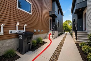 Ein Wohngebäude mit modernem Design, mit Holzfassade, Betonweg und einem roten Pfeil als Wegweiser.