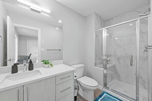 Une salle de bain moderne avec une douche à parois de verre, des toilettes blanches, un meuble-lavabo avec un miroir et une petite plante posée sur le plan de travail.