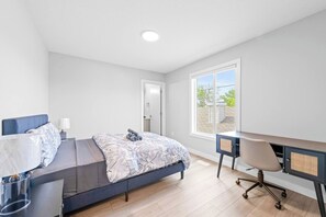 Ein modernes Schlafzimmer mit Bett, Schreibtisch und Stuhl, einem Fenster mit Blick und einer Tür.