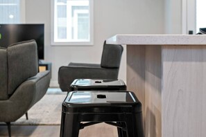 A modern interior with a kitchen counter, two black stools, and a grey sofa. - 5BR Townhouse | 4 Ensuites | Near UofA, Whyte & DT (Edmonton)