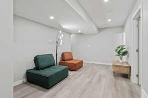 A modern interior with a green sofa, a brown ottoman, and a wooden side table with a plant. - 5BR Townhouse ● 4 Ensuites ● Near U of A, Whyte & DT (Edmonton)