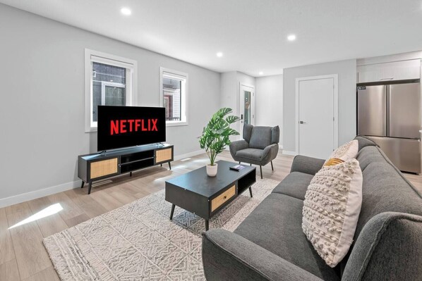 Un salon moderne avec un téléviseur à écran plat, un canapé gris, une table basse et une plante en pot.