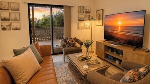 Una sala de estar con sofá, sillones, una mesa de centro y una televisión que muestra una vista al atardecer.