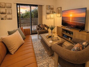 Un soggiorno con divano, poltrone, tavolino e televisione che mostra una vista sul tramonto.