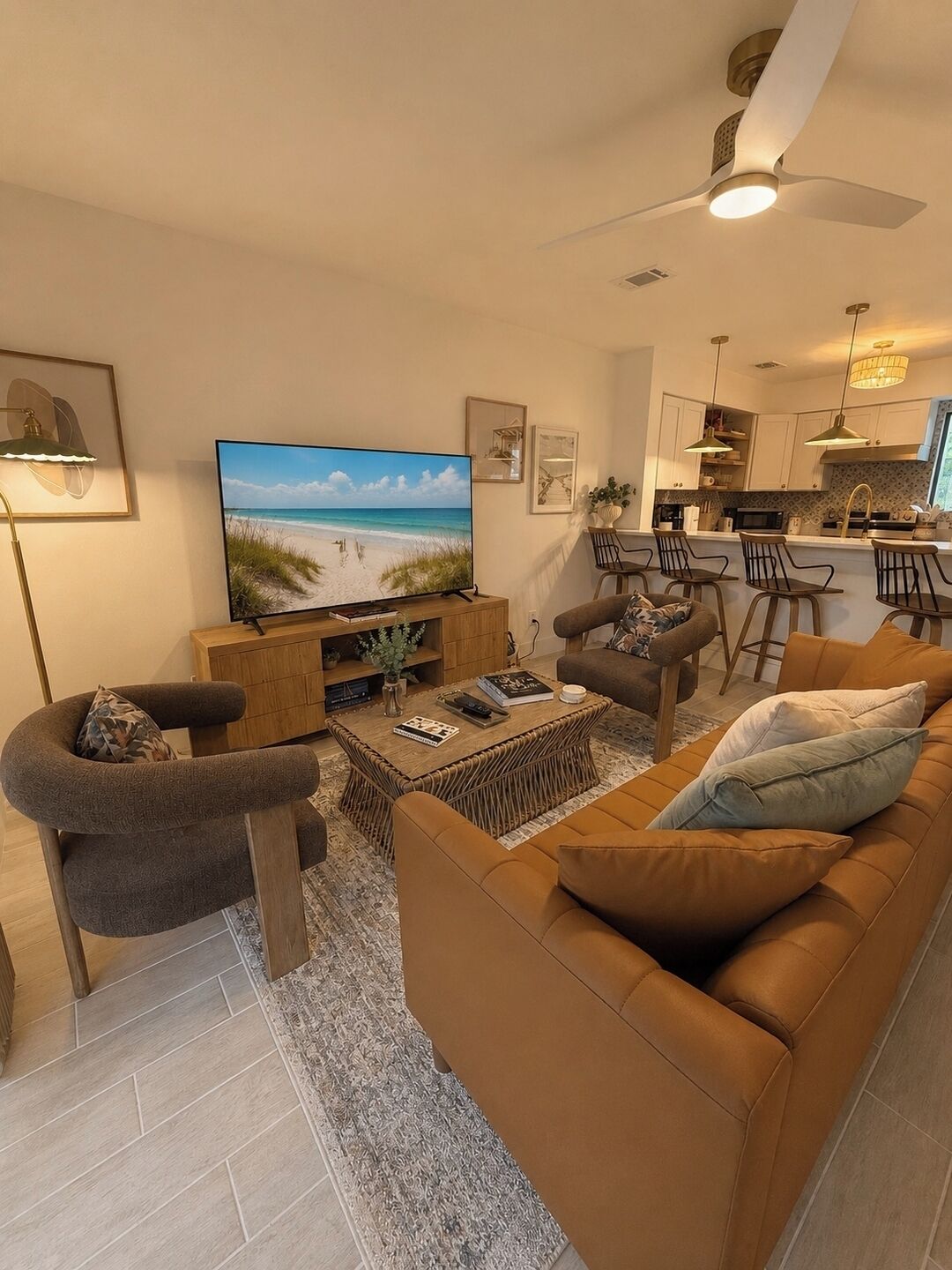A modern living room with a flat-screen TV, comfortable seating, and a kitchen area in the background.