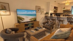 Una sala moderna con un televisor de pantalla plana, asientos cómodos y una cocina al fondo.