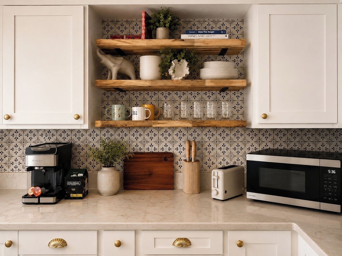 Una cucina con mobili bianchi, una macchina da caffè, un tostapane, un forno a microonde e oggetti decorativi sugli scaffali.