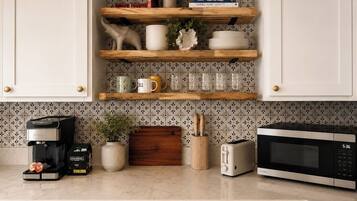 Una cucina con mobili bianchi, una macchina da caffè, un tostapane, un forno a microonde e oggetti decorativi sugli scaffali.