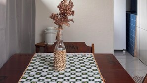 A dining area with a table covered by a patterned tablecloth, a vase with dried flowers, and two wall-mounted decorative items. - Stone Retreat Paraty (Paraty)