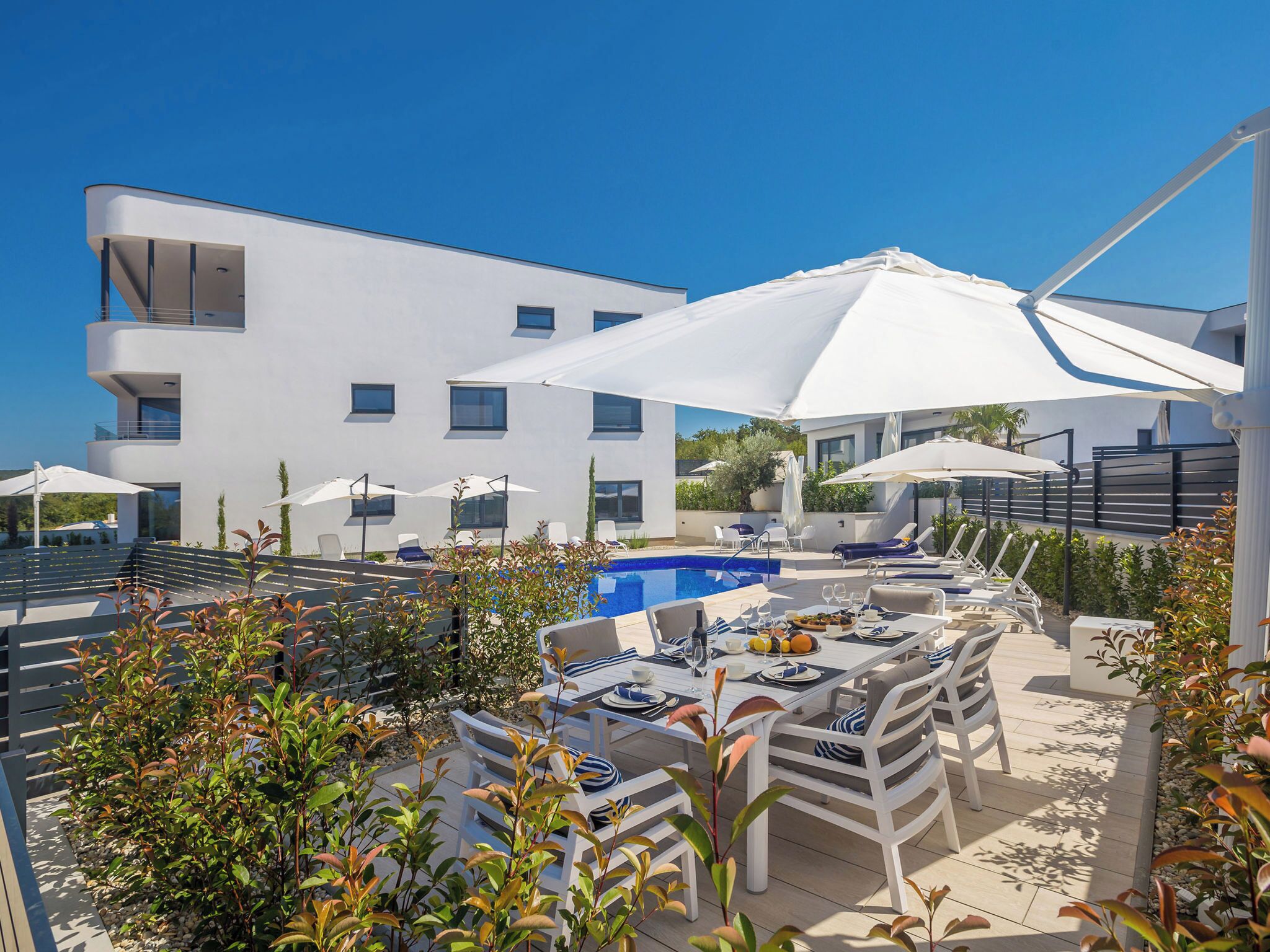 A modern building with a pool, outdoor seating, and umbrellas.