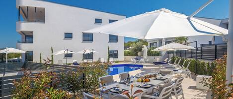 A modern building with a pool, outdoor seating, and umbrellas.