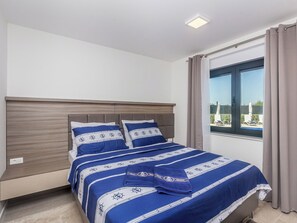 A bedroom with a bed, a headboard, a window with curtains, and a view of the outside. - Apartment Poseidon - 1 by Interhome (Krk/Milohnići)