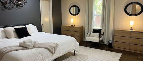 A bedroom with a large bed, two bedside tables with lamps, a chair, and a mirror on the wall.