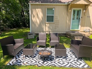 A patio with wicker furniture, a fire pit, and a patterned rug. - The Cityside Villa of KC - 10 min from Downtown and Stadiums (Raytown)