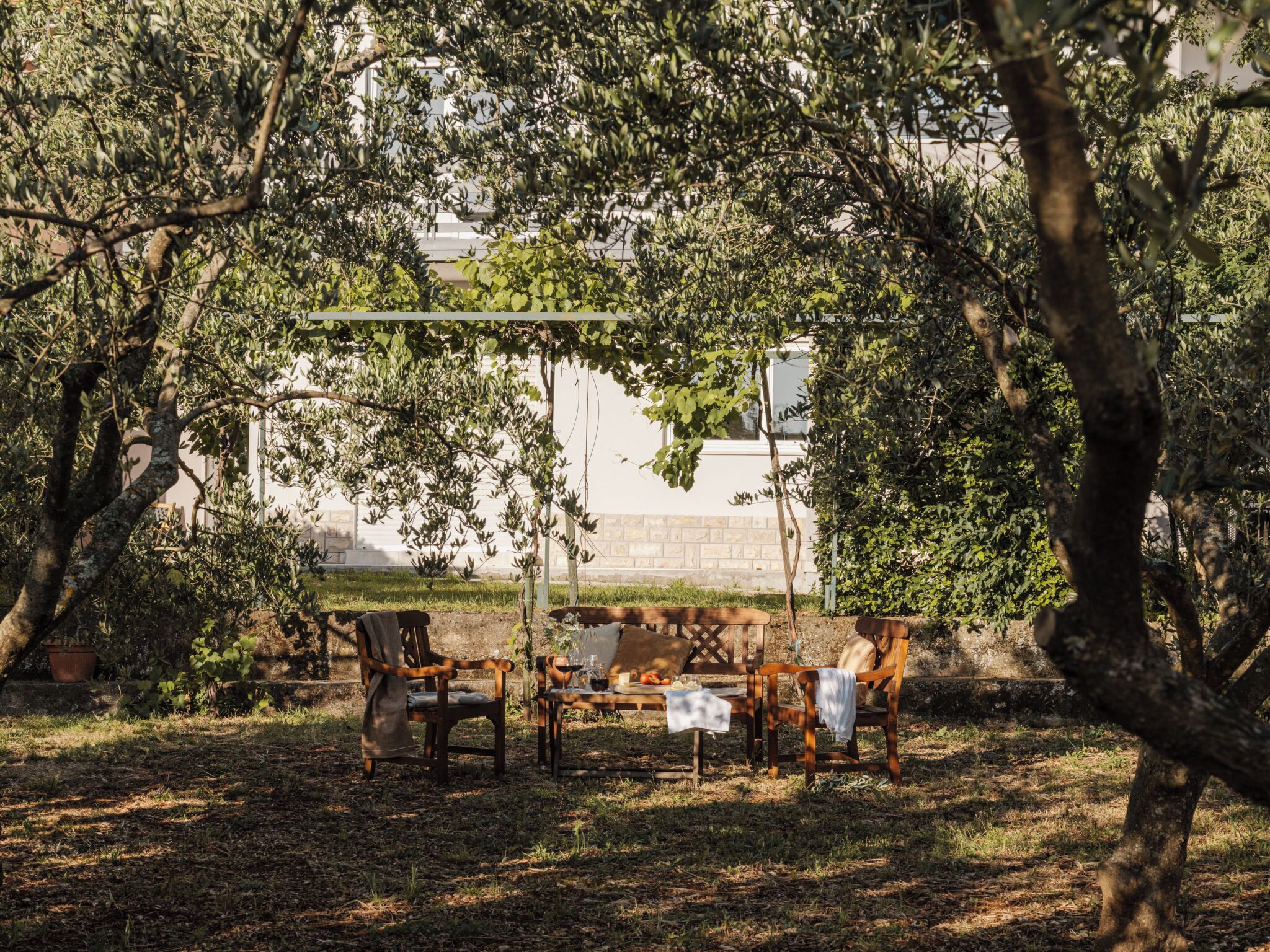 An outdoor seating area with a bench and table, surrounded by trees and a stone wall.
