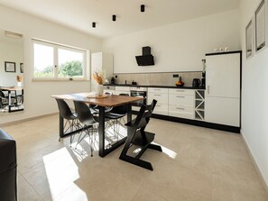 A modern kitchen with a dining area, featuring a wooden table, black chairs, white cabinets, and a black range hood. - Apartment Silvana - 1 by Interhome (Krk/Milohnići)
