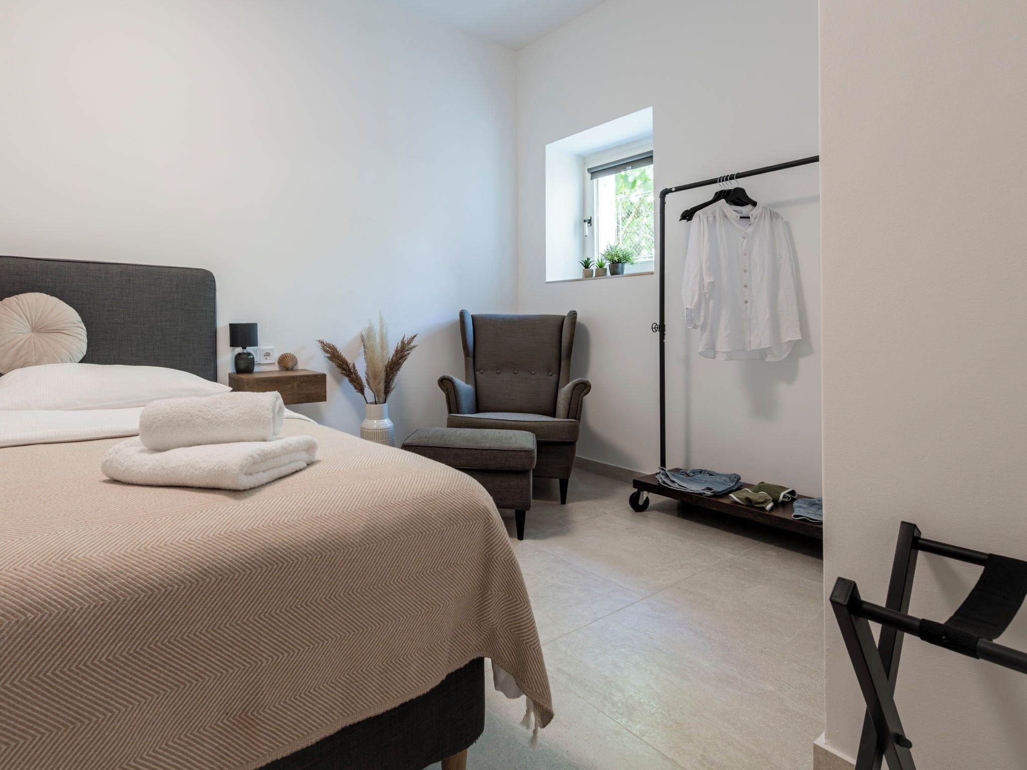 A bedroom with a bed, a chair, a clothing rack, and a window.
