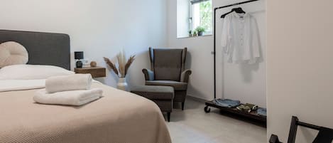 A bedroom with a bed, a chair, a clothing rack, and a window.