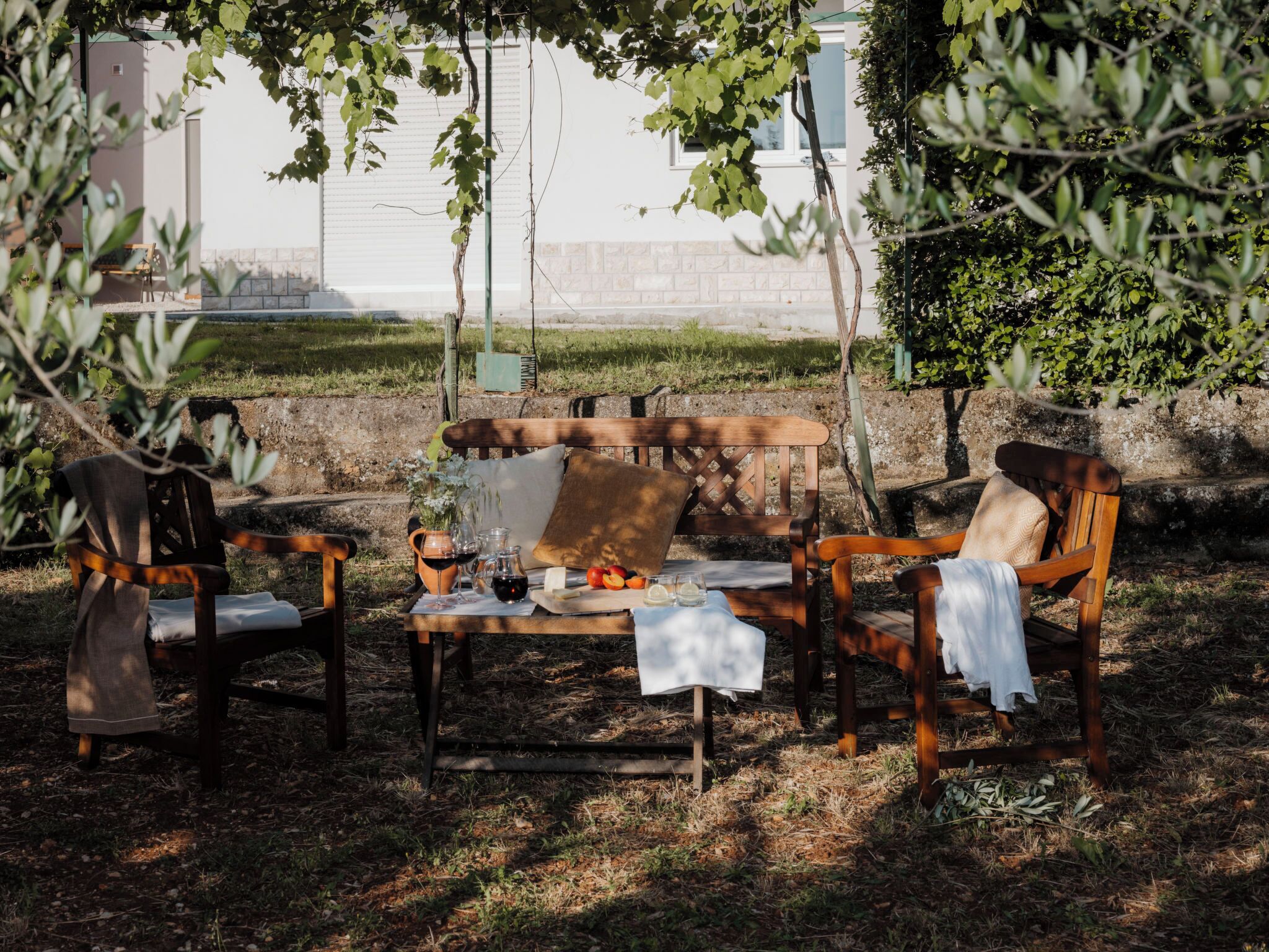 An outdoor seating area with a wooden table and chairs, a wine bottle, glasses, and a fruit plate.