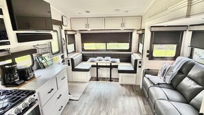A compact RV interior with a kitchenette, dining area, and seating space.