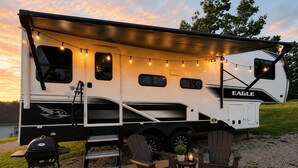 A recreational vehicle with a covered deck area, a grill, and outdoor seating.