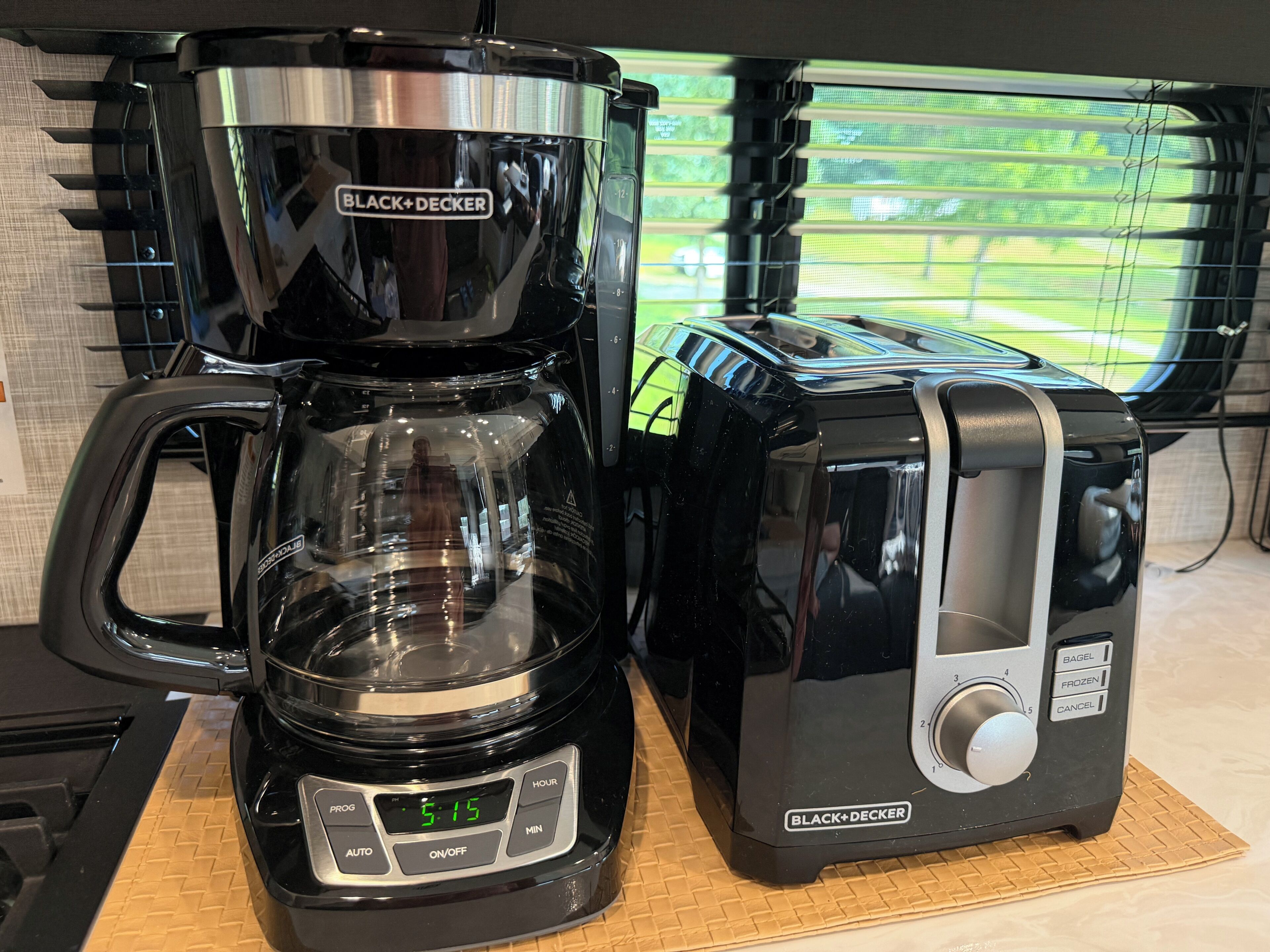 A BLACK+DECKER coffee maker and toaster on a countertop with a window in the background.