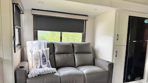A compact living space with a cushioned seating area, a window with a view, and a black refrigerator.